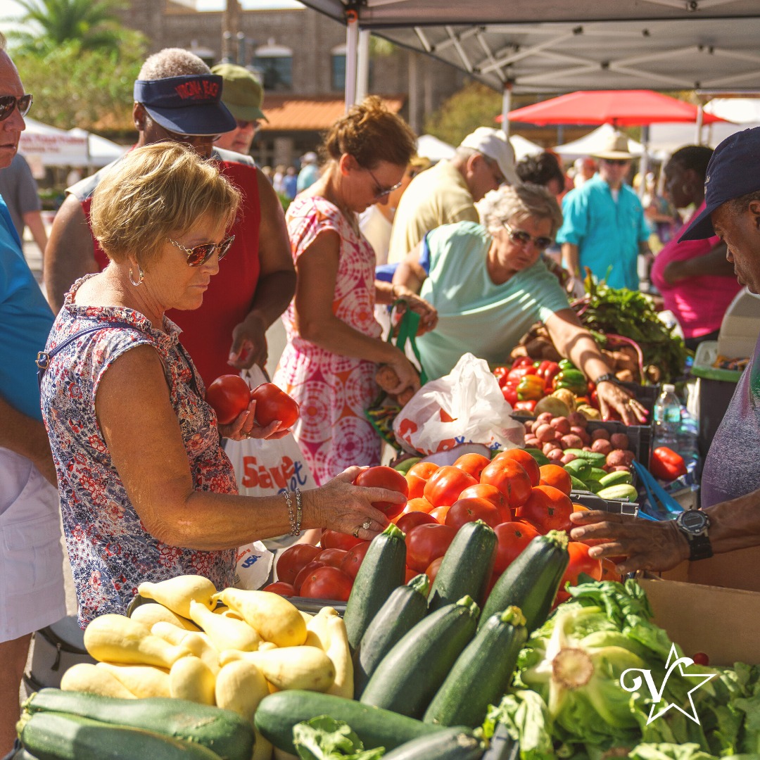 A colorful market scene with people browsing and shopping for food items.