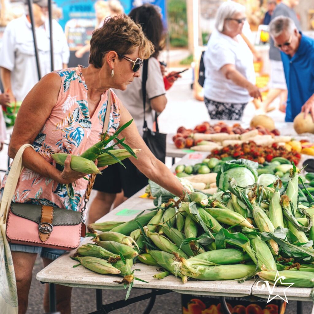 People gathered around a stall at an outdoor market, with a focus on fresh produce.