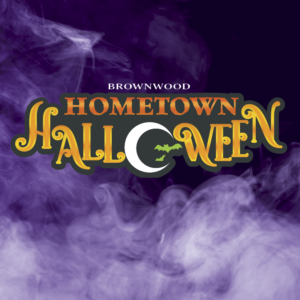 A smokey purple background with a logo that reads "Brownwood Hometown Halloween." The "o" in "Halloween" is a crescent moon containing green bats.