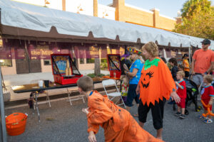 Patrons playing carnival games at hometown Halloween dressed up in costumes like pumpkins