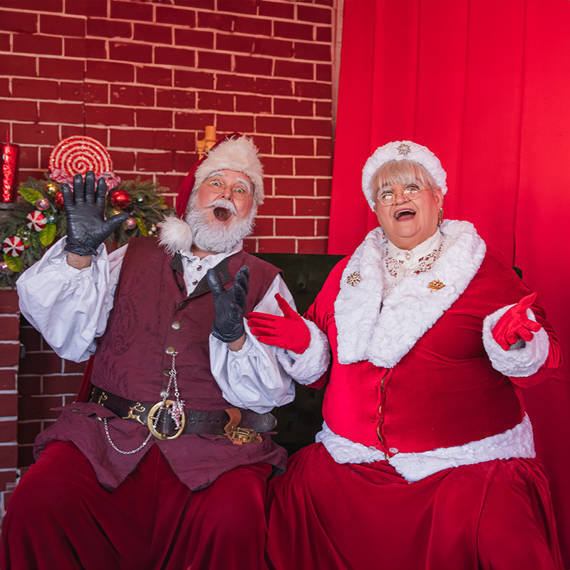 Mr. & Mrs Claus in santa village sitting in a chair excited to greet people