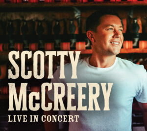 Country artist Scotty McCreery smiling in a white t-shirt with text “Scotty McCreery Live in Concert.”
