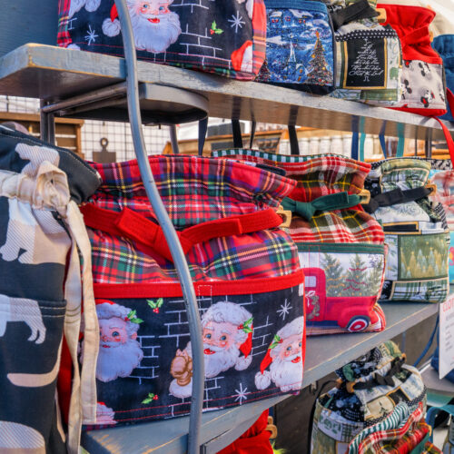 Shelves displaying cloth totebags, mostly Christmas themed.