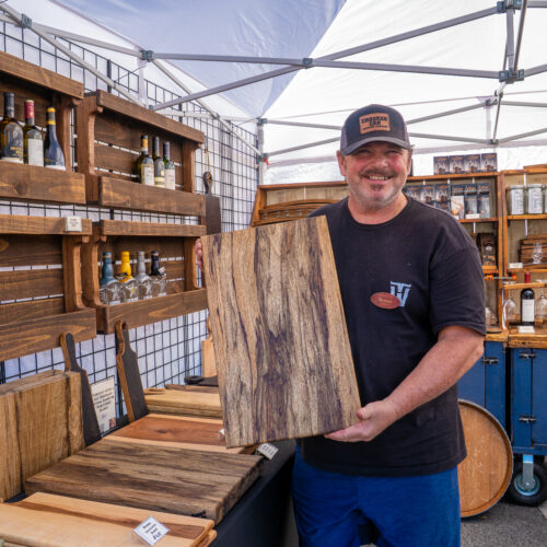 A man is holding his large wooden cutting board he crafted.