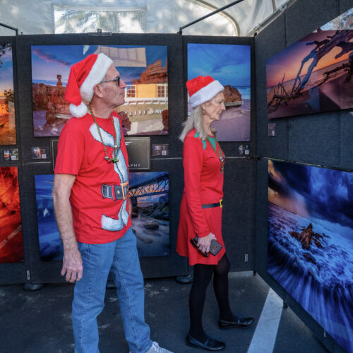 A man and a woman dressed in coordinating Santa outfits view a gallery of fine art photography.