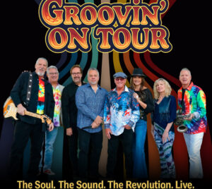 A large funk and soul band stands together across the foreground against a bold, retro‑inspired backdrop of curved, multicolored stripes radiating outward. The performers wear vibrant, patterned stage outfits in bright hues, with visible instruments including electric guitar and saxophone. At the top, large stylized lettering reads “Groovin’ On Tour.” Along the bottom, yellow text reads “The Soul. The Sound. The Revolution. Live.”