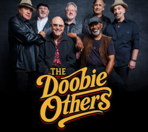 A group of seven performers is posed together against a dark, studio-style background. The performers wear coordinated, classic rock–inspired clothing including leather jackets, vests, button‑down shirts, and hats. The arrangement is layered, with some performers standing and others seated in front, creating a balanced band portrait composition. Centered near the bottom is a large, retro‑styled logo reading “The Doobie Others” in bold yellow and orange lettering with a curved, vintage design.