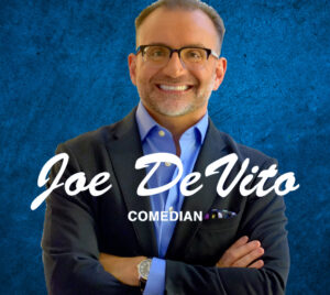 A person stands with arms crossed, wearing a dark blazer over a blue dress shirt with a pocket square, against a textured blue background. Large white script text across the center reads “Joe DeVito,” with smaller uppercase text below reading “Comedian.”