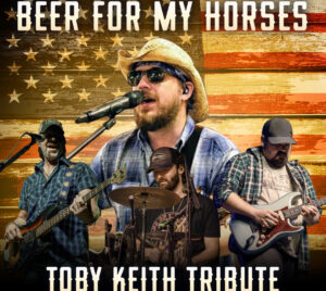 The background features a distressed American flag in warm red, tan, and gold tones. In the foreground, a country band is pictured with a central singer at a microphone, flanked by musicians playing electric guitar, bass guitar, and drums. The performers wear casual, country‑style clothing including plaid shirts and hats. Bold white text at the top reads “BEER FOR MY HORSES,” and matching text at the bottom reads “TOBY KEITH TRIBUTE.” The overall design conveys a patriotic, high‑energy country music concert atmosphere.