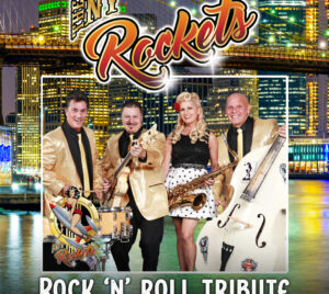 The background shows a nighttime city skyline with illuminated skyscrapers and a suspension bridge reflected on water. In the foreground, a rock‑and‑roll band poses together, with three males wearing matching gold jackets and black attire and one female wearing a black lace top and a white skirt with black polka dots. Visible instruments include a snare drum, electric guitar, saxophone, and an upright bass. At the top, stylized script text reads “The NY Rockets.” At the bottom, bold white lettering reads “Rock ’N’ Roll Tribute.” A small illustrated pin‑up style graphic appears near the lower left, reinforcing a retro rock‑and‑roll theme. The overall design evokes a high‑energy, vintage rock tribute concert aesthetic.