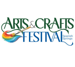 "Arts & Crafts Festival - Spanish Springs." "Arts" and "Crafts" are in green text above "Festival" in blue text. The words are intersected by a paintbrush with rainbow paint. The location is mentioned in blue text next to the word "Festival."