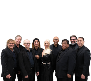 Groove Slayers, a female fronted band of 9, pose and smile. All members are wearing black.