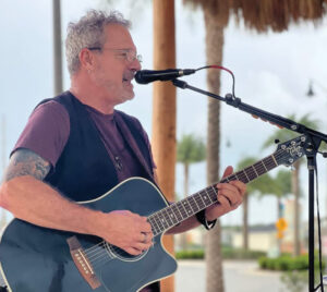 Thomas Watkins singing and playing an acoustic guitar.