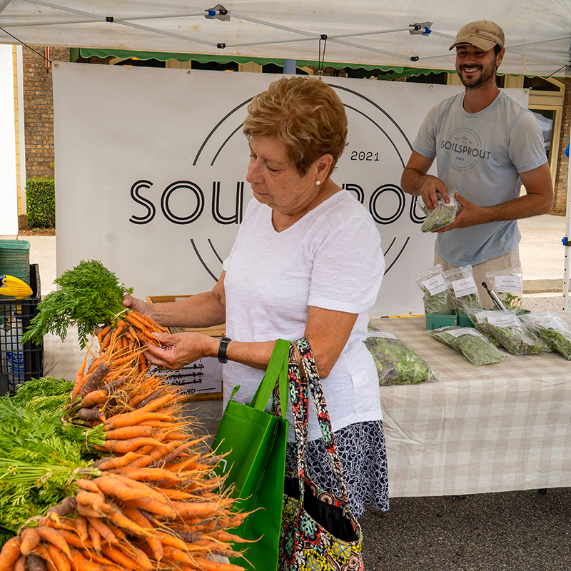 The vendor for Soul Sprouts looks delighted as a patron assesses a bundle of carrots.