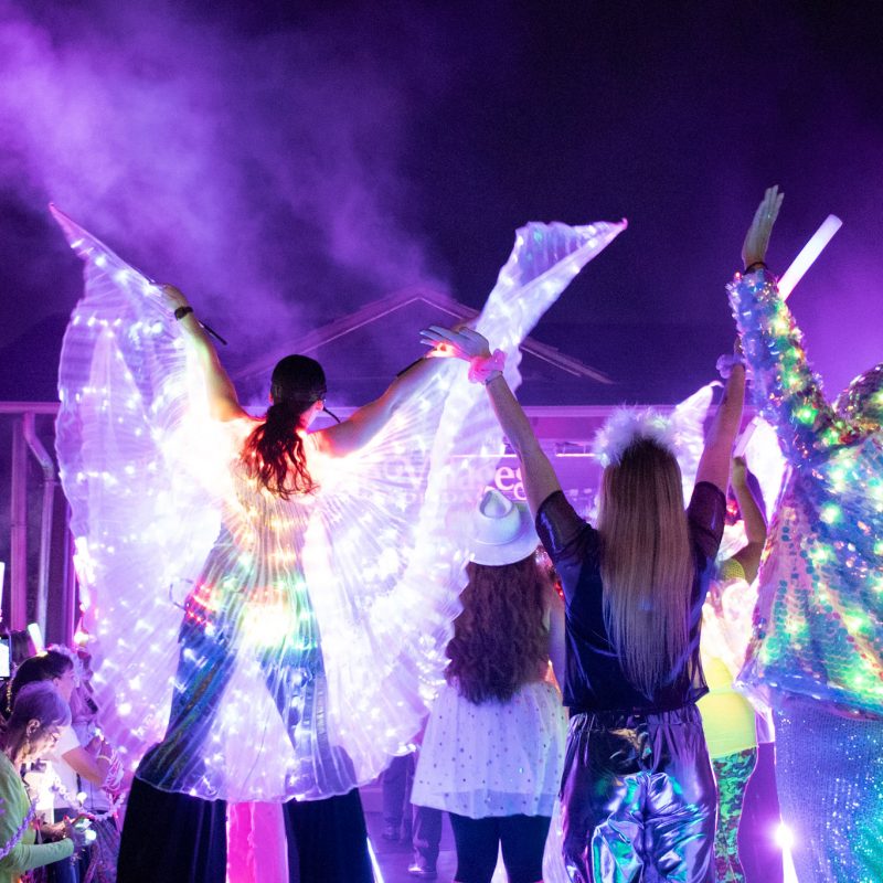Crowd photo of a group of people all dressed up for electric light party with their hands in the air enjoying the music